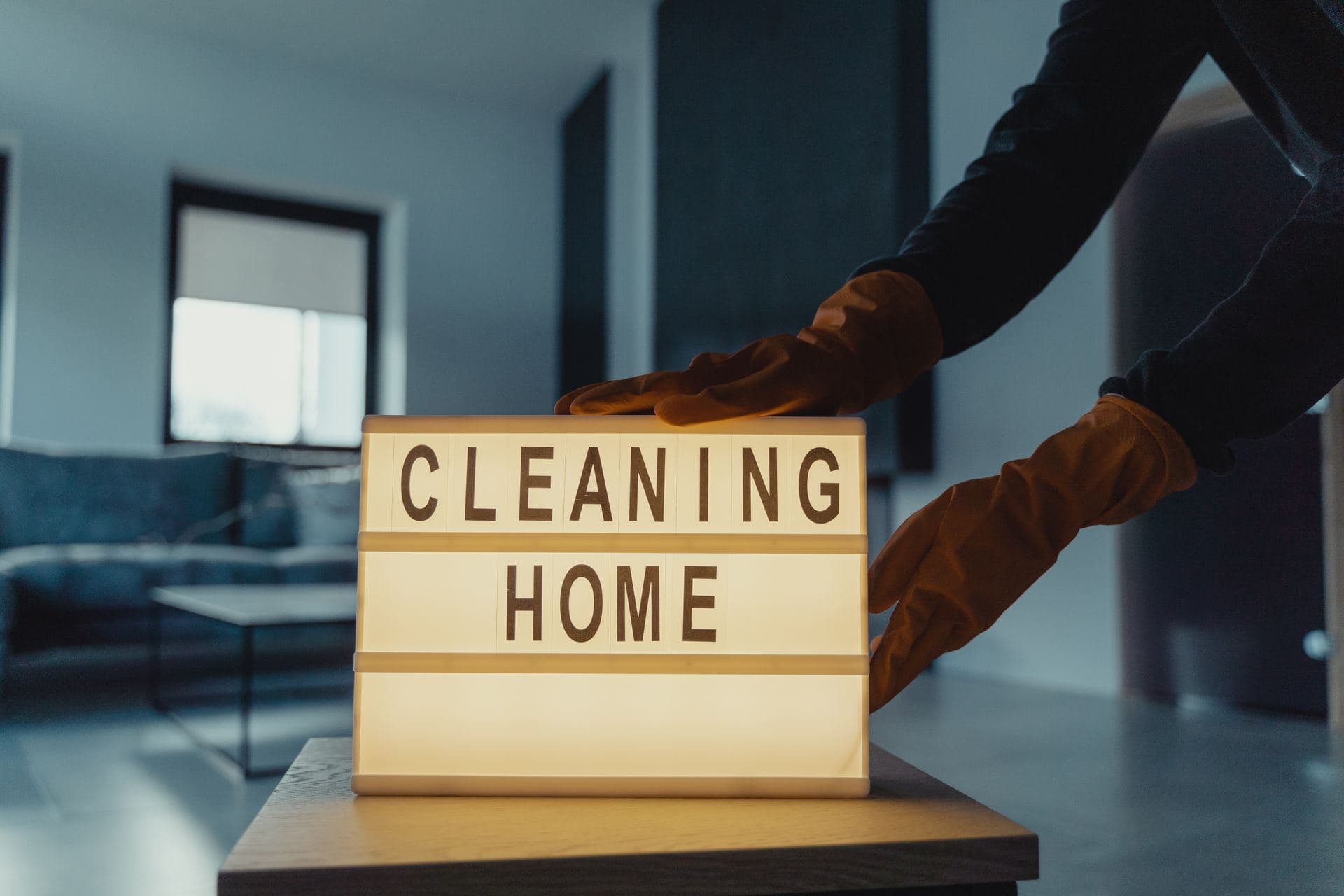 Gloved hands placing a Cleaning Home sign in a living room