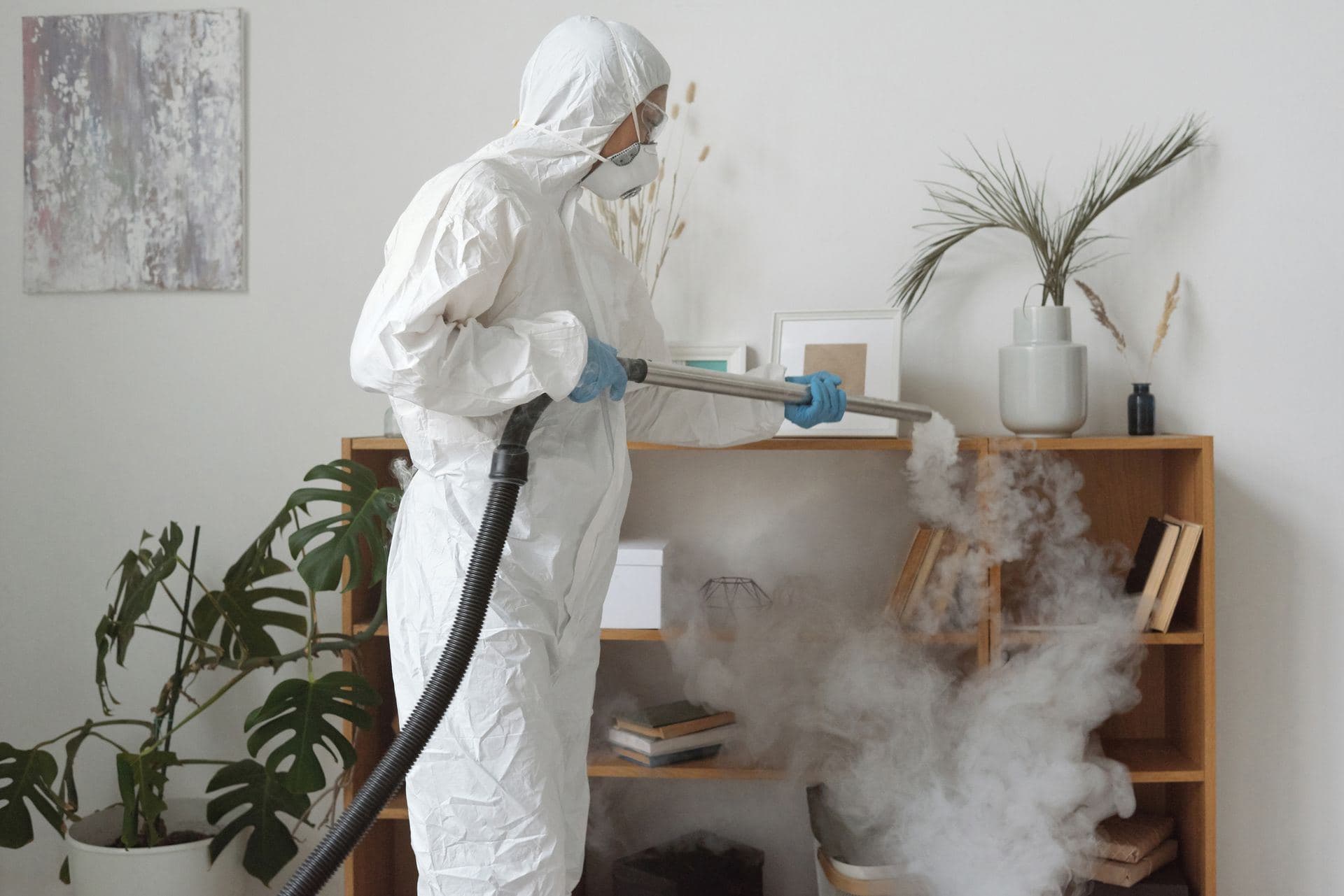Technician in a protective suit steam-disinfecting a room